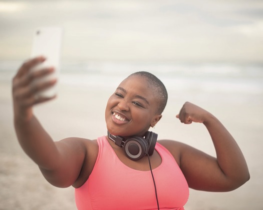 Selfie, flexing and plus size black woman at beach for health, fitness or cardio. Smile, exercise or sports and bicep muscle of happy young running athlete outdoor for strength training or workout