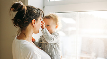 Mother holds toddler as toddler playfully grabs mother's nose. 