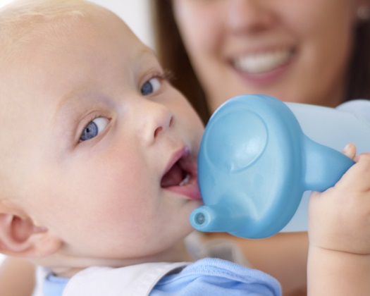 Portrait of a young mother handing her baby boy his sippy cup filled with water