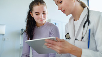 Healthcare professional sharing a tablet and in discussion with an adolescent girl.