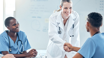Healthcare providers of various specialties and backgrounds gathered around a table and two are in a handshake.