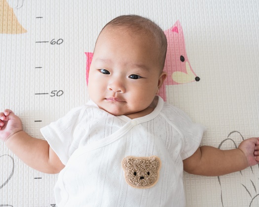 An Asian baby playing alone on a crawling mat