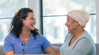 Healthcare professional and patient with cancer in conversation in a sunny indoor environment.
