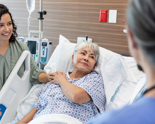 A view over the shoulders of two unrecognizable emergency room doctors in the foreground of a cheerful young adult woman supporting her very sick senior adult mother.