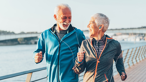 Senior couple in sports clothing and sports technologies jogging together across the bridge